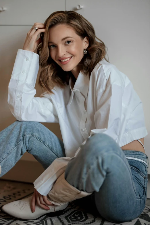 a woman in a white shirt and blue jeans sitting on the ground