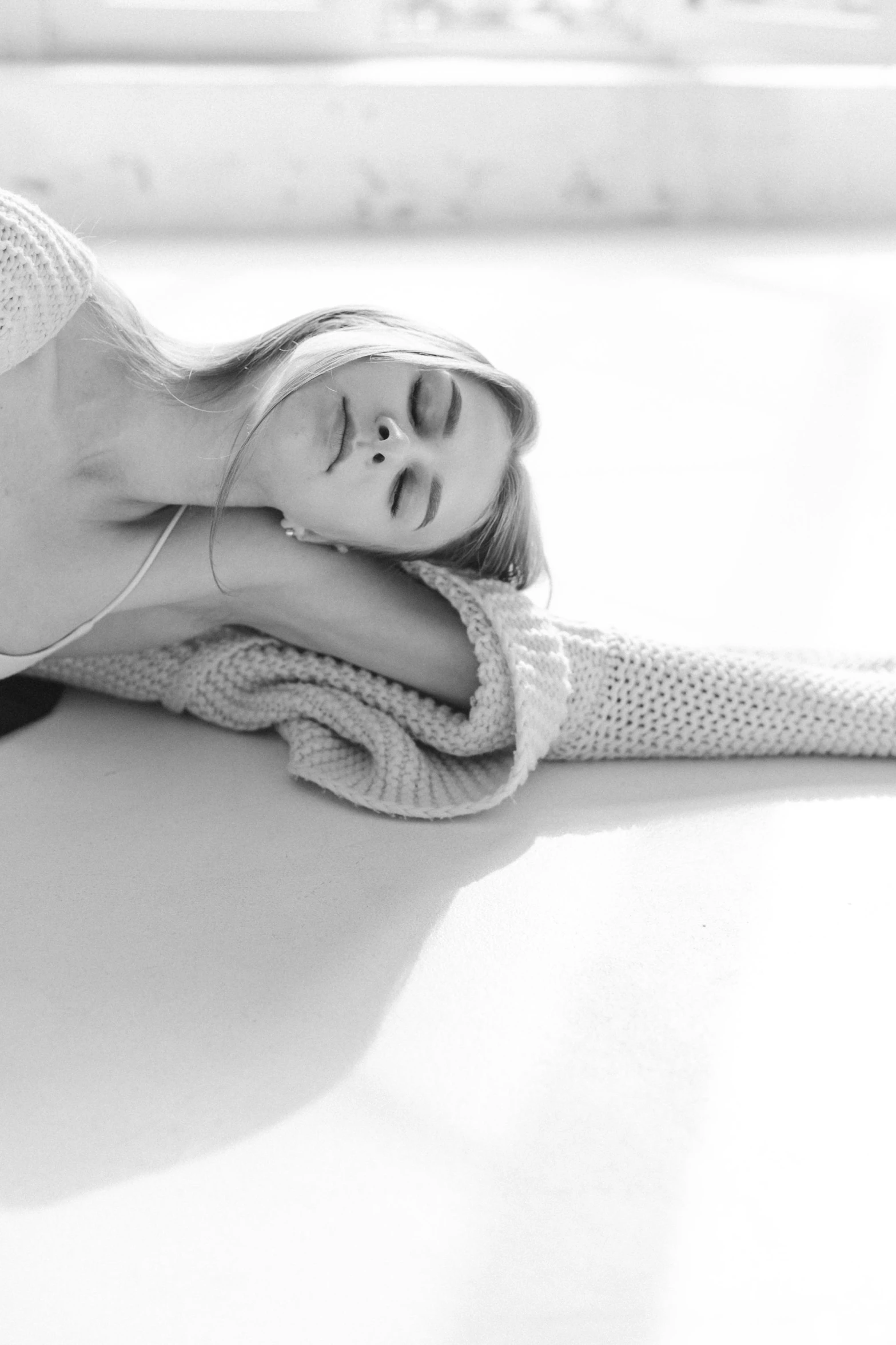 black and white pograph of a woman in white sweater laying on a floor with headphones
