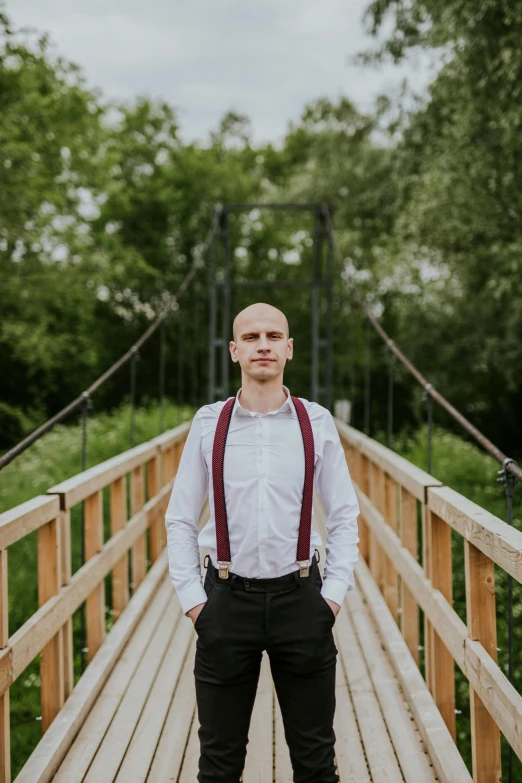 a man is standing on a bridge wearing suspenders and a bow tie