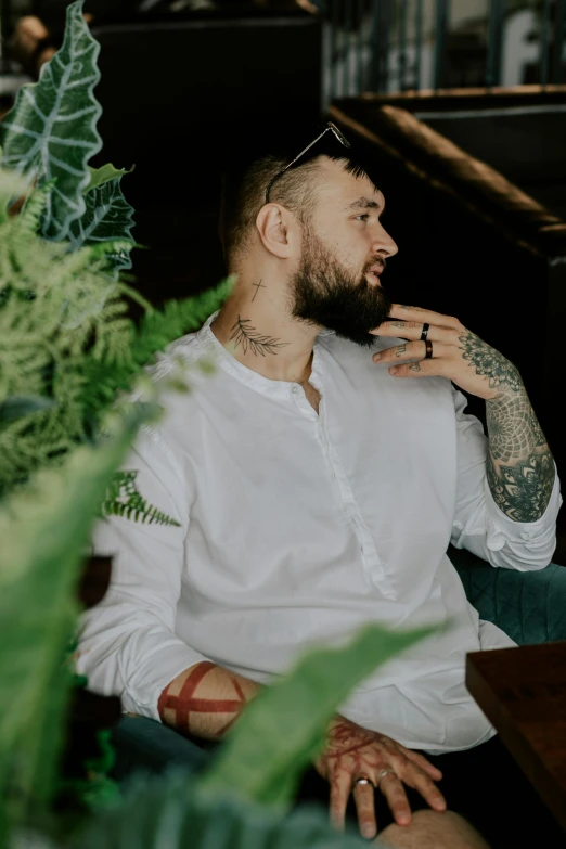 tattooed man with white shirt and hair tie seated and looking away from the camera