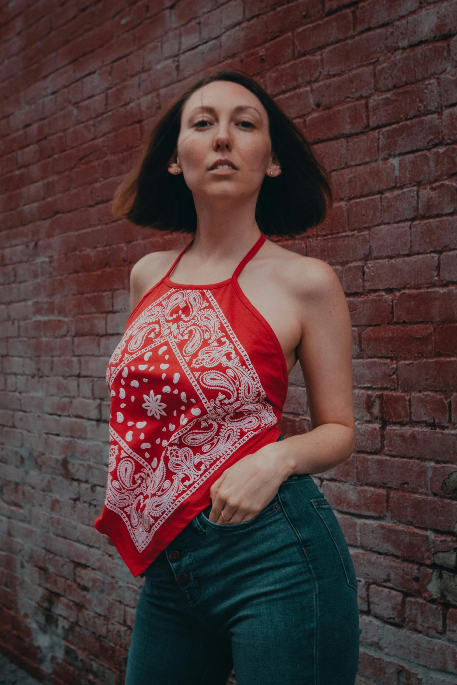 a woman in a bandana poses next to a brick wall