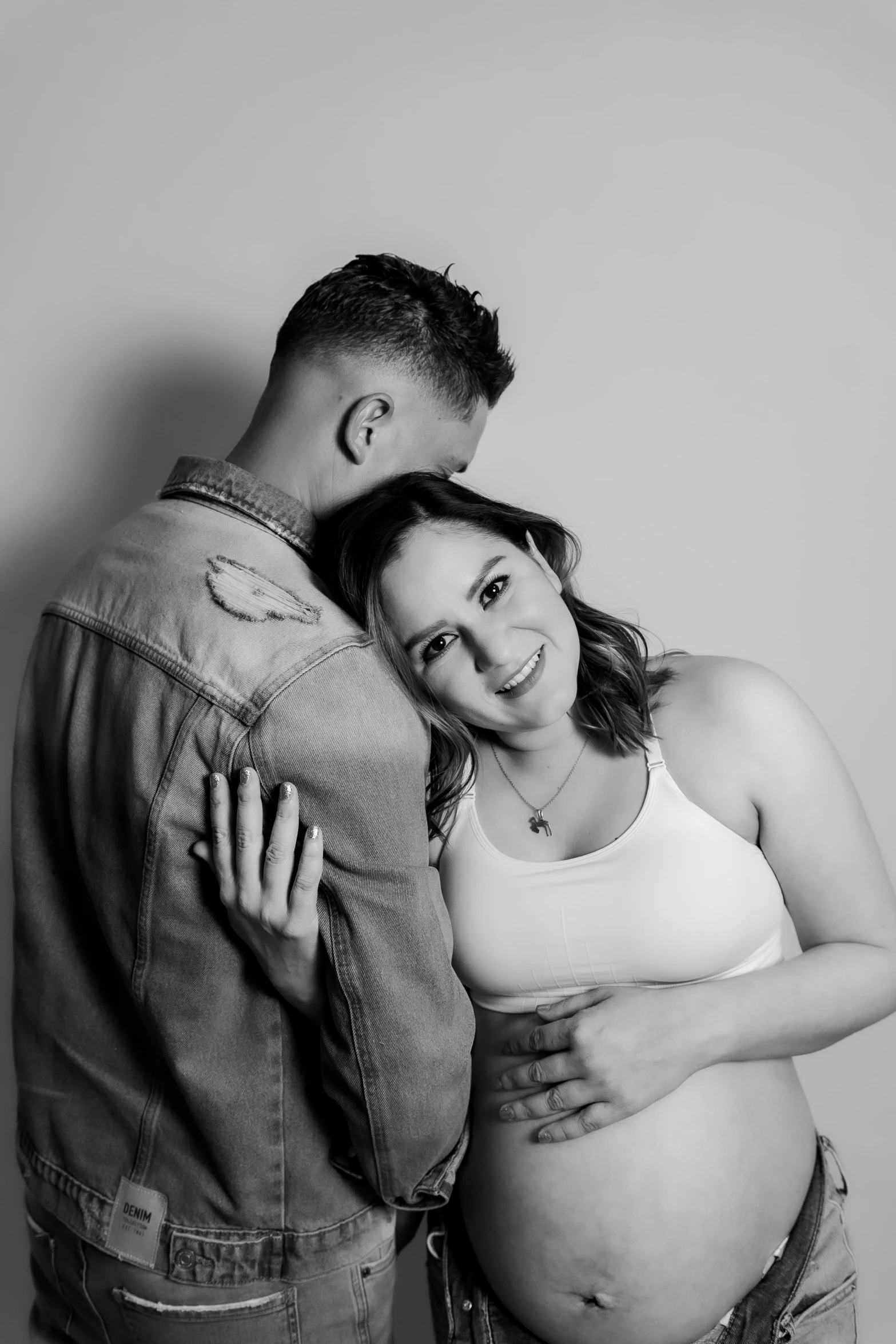 a pregnant couple hugging and cuddling while wearing jeans