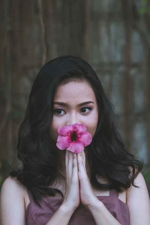 the woman is hiding her face in front of her hands with the pink flower in her mouth