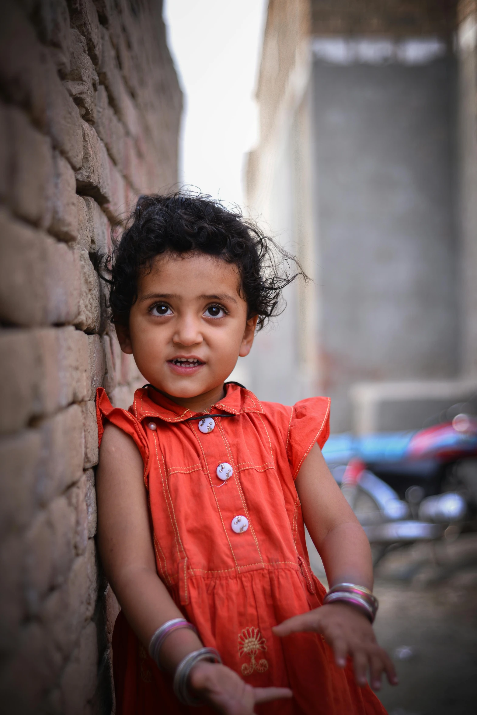 a young indian girl leans against a brick wall