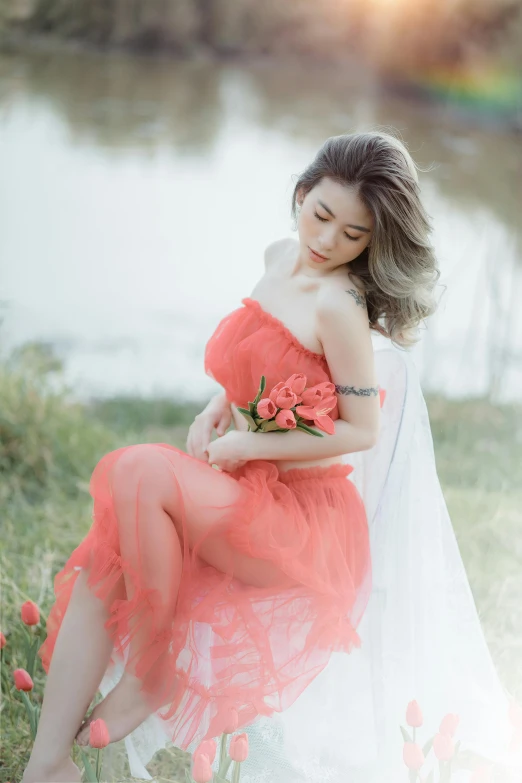 woman in dress sitting by water holding flowers