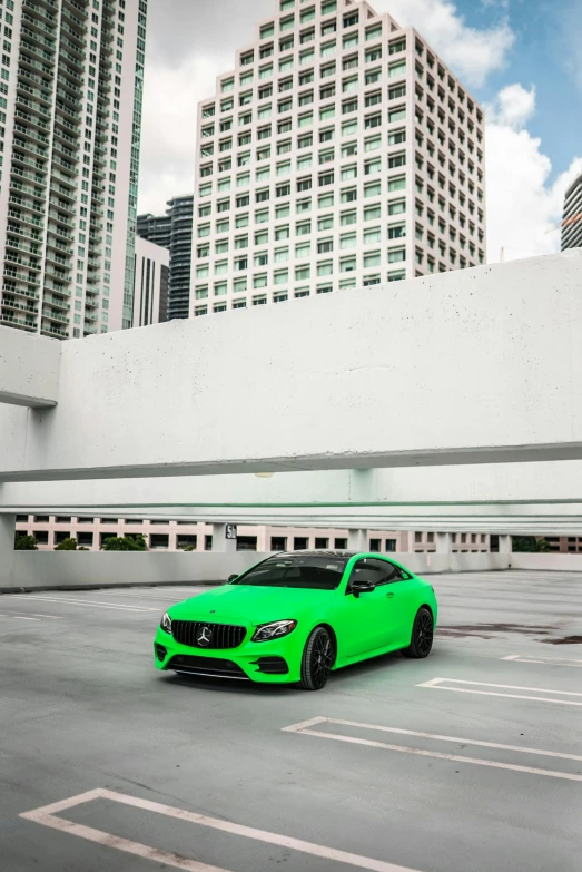 green mercedes benz coupe car in parking lot with large skyscrs