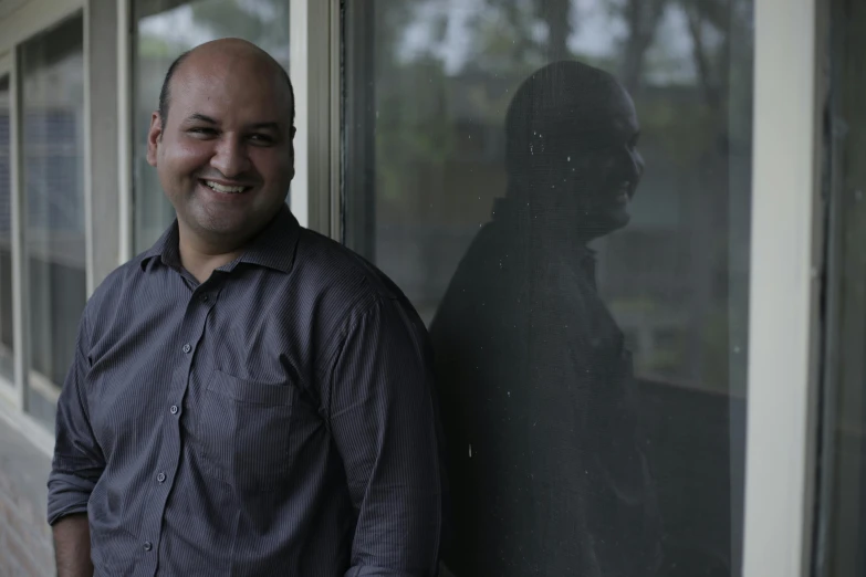 a man with a shaved head is standing in front of a window