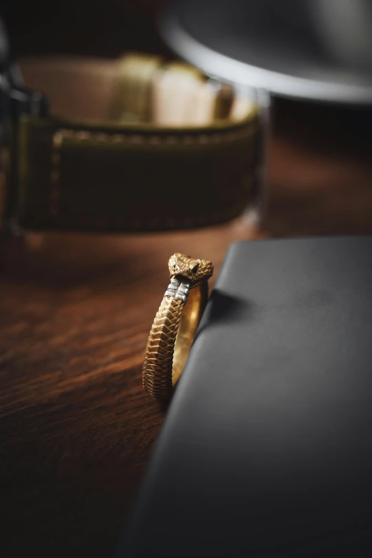 a golden snake ring is on top of a leather wallet