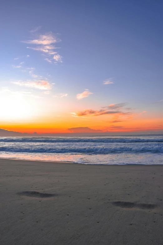 footprints walking on the sand and water of an ocean at sunset