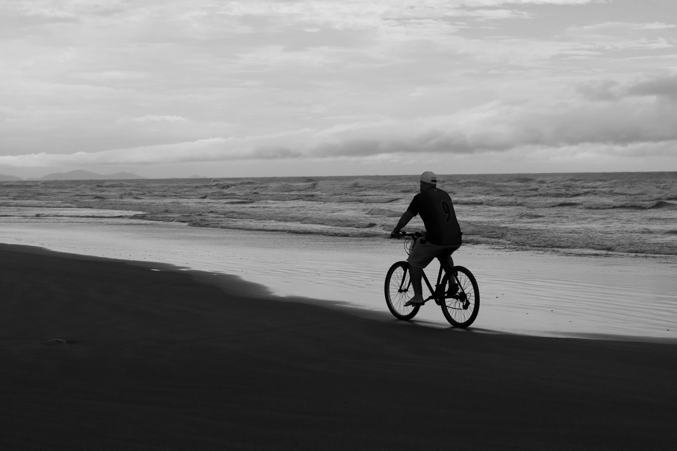 man riding bicycle along the shoreline of a large body of water