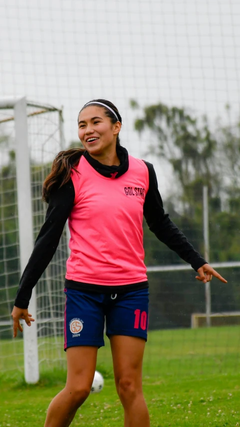 woman playing soccer wearing a pink top and blue shorts