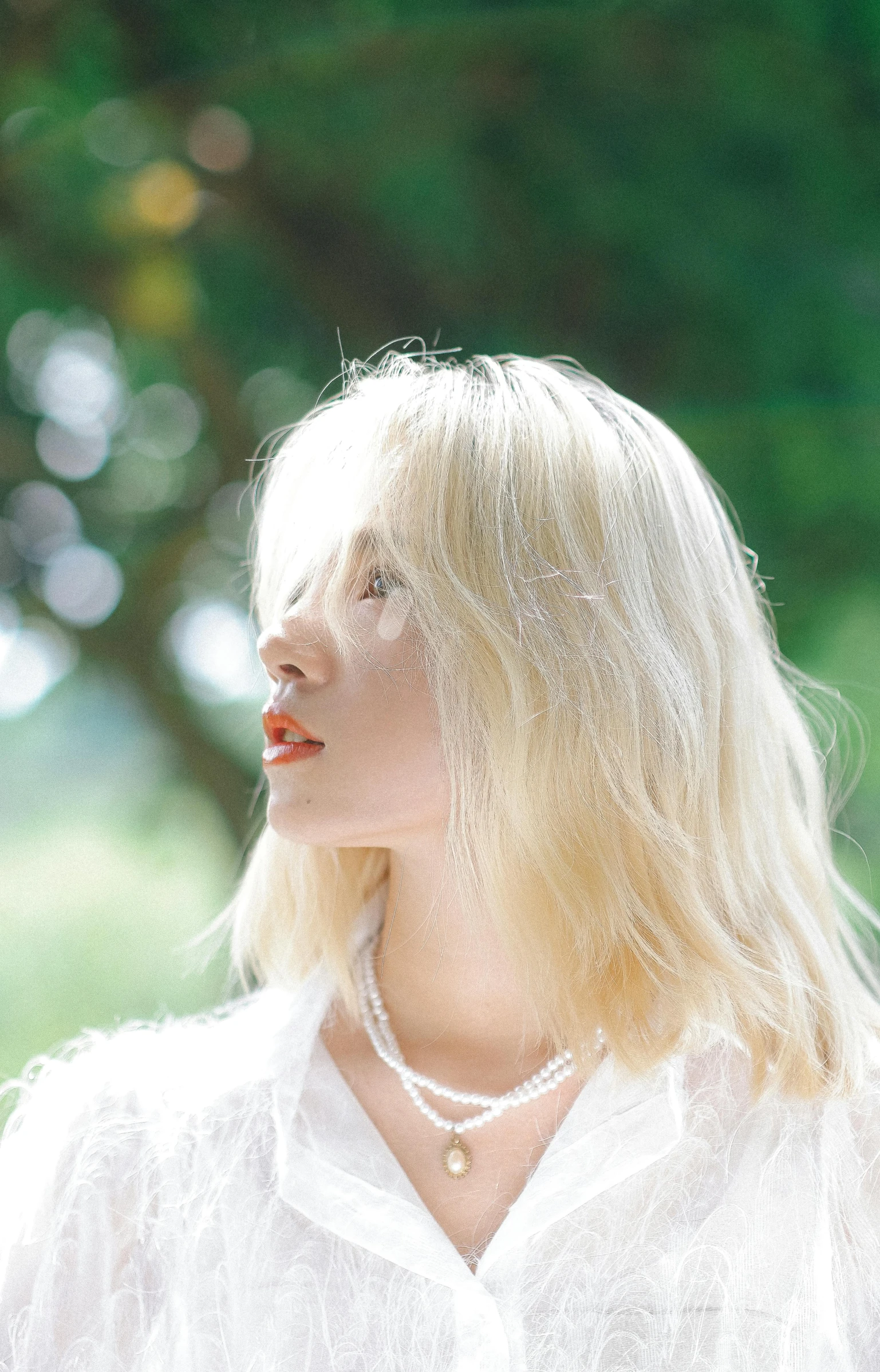 a woman with blonde hair and a pearl necklace looks away