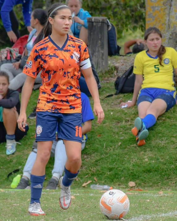 a female soccer player in an orange jersey is about to kick the ball