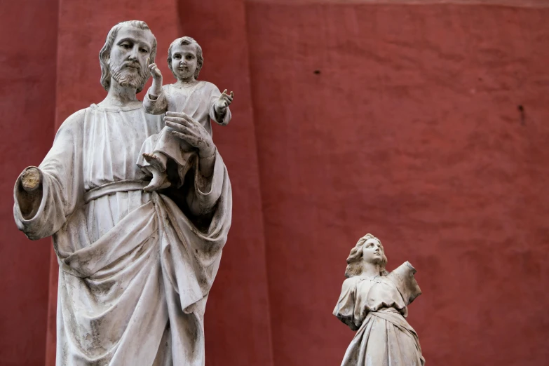 a statue of jesus, a child and a woman are posed in front of a red backdrop