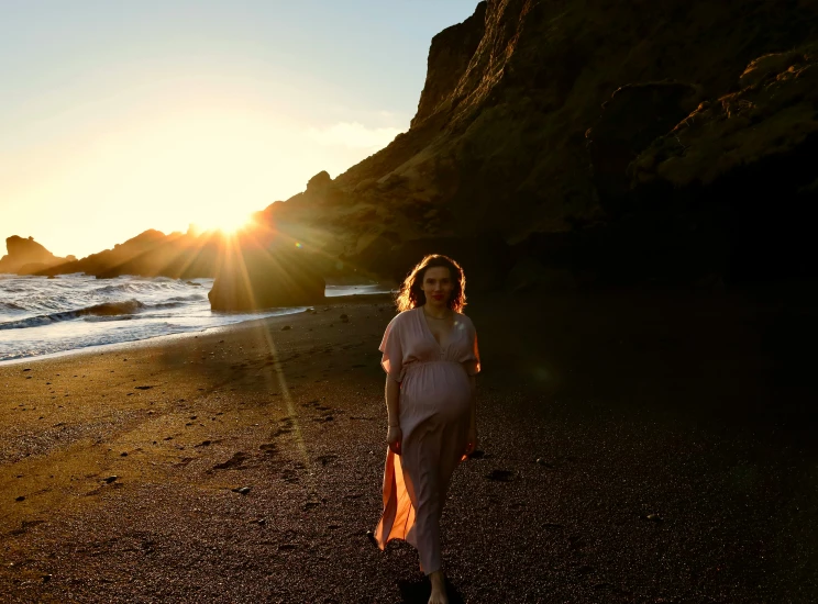 a woman stands on the beach, with the sun behind her