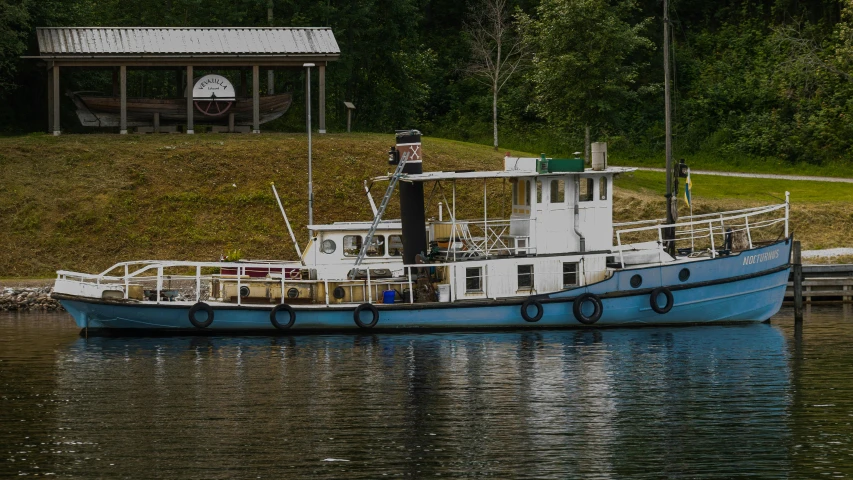 a blue boat floating on top of a river next to a shore