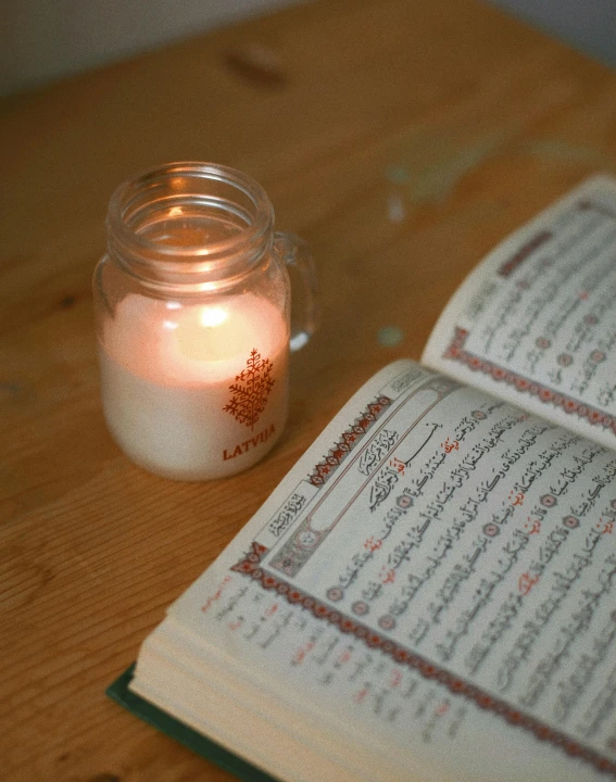 an open book sitting on a desk next to a lit candle