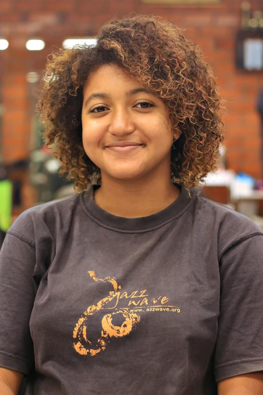 a girl with curly hair and a brown t shirt smiling at the camera