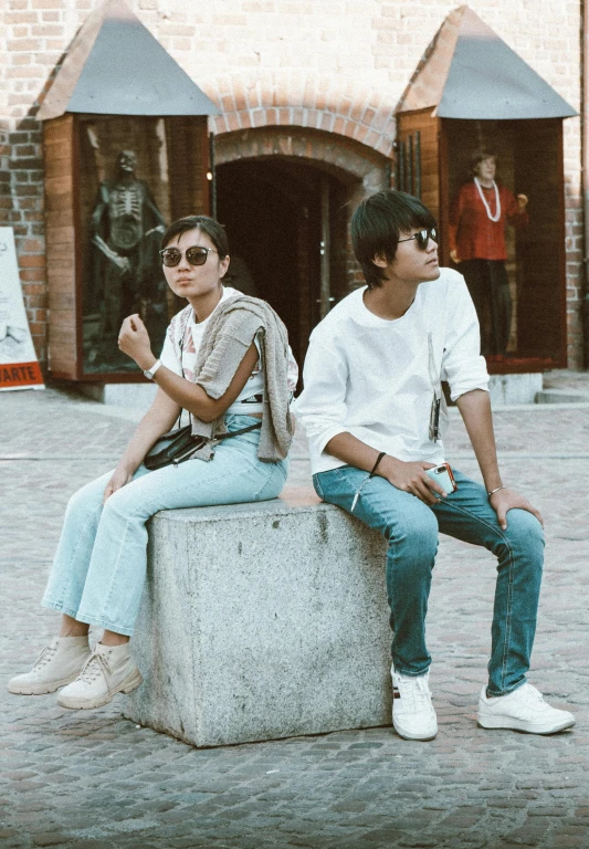 two young people sitting on top of a cement block