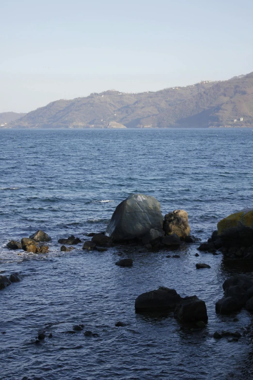 a large rock is sitting on the shore line near the water