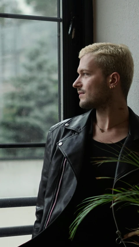 a young man leaning against a window near a plant