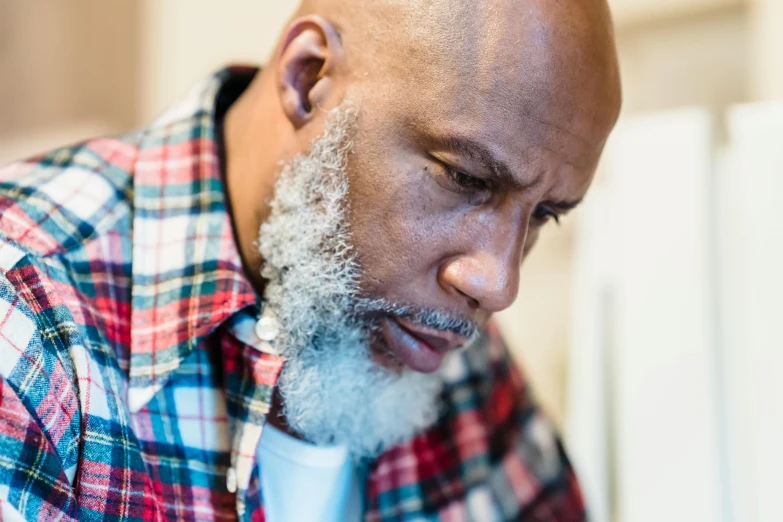 an african american man with a bald head wearing plaid shirt looks into a camera