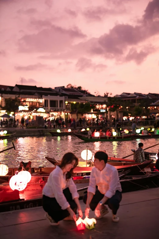 a couple of people standing next to a lake at dusk