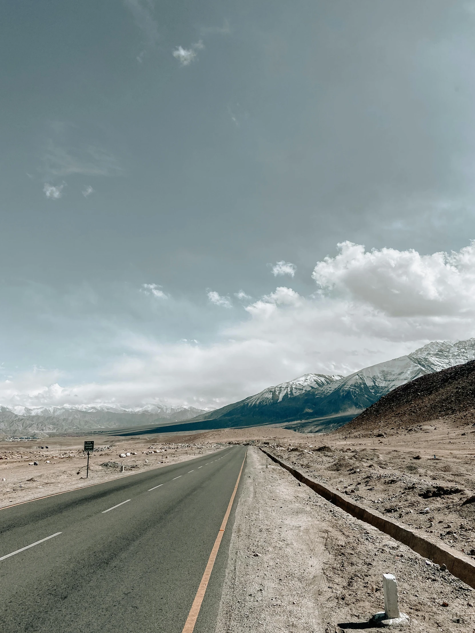 a lone person walking on the side of a road with snow covered mountains behind them