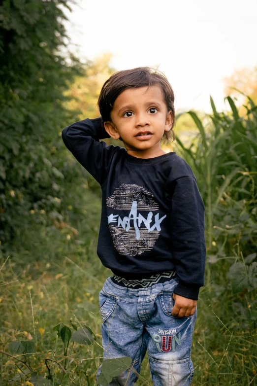 a young child standing in a grassy area, wearing a blue sweatshirt
