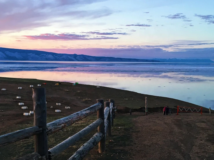 people are walking near the water at sunrise