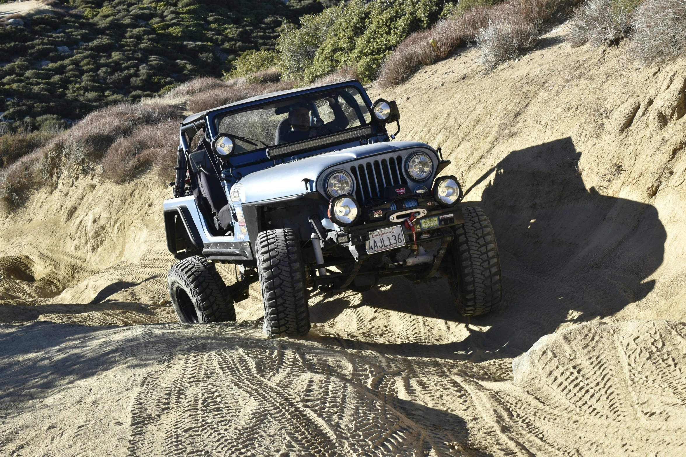 a black jeep with an old style grill and a hard - top driving down a trail in the mountains