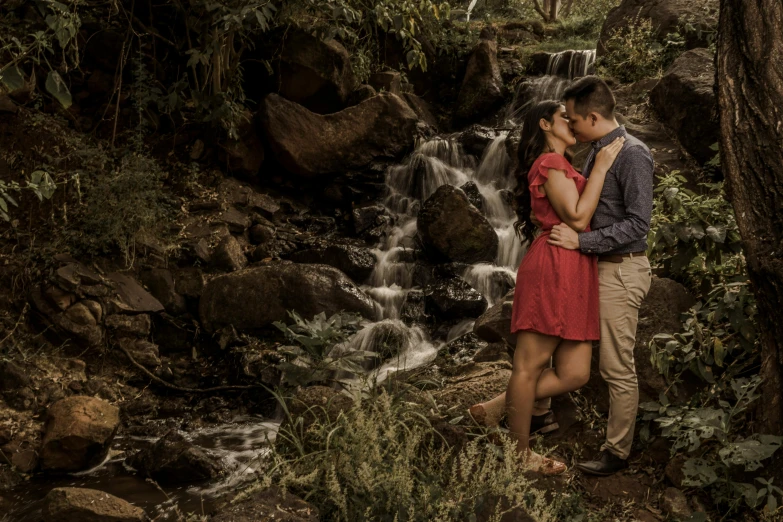 there is a man and woman kissing in front of a waterfall