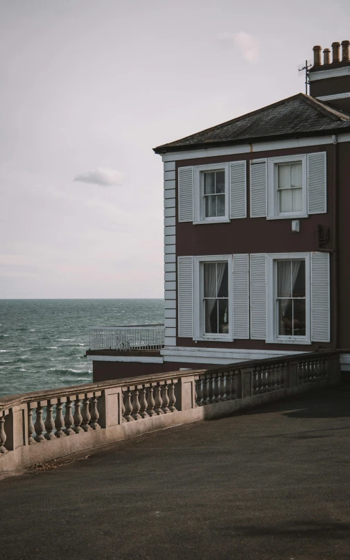 an empty sidewalk near the ocean by a house with white shutters