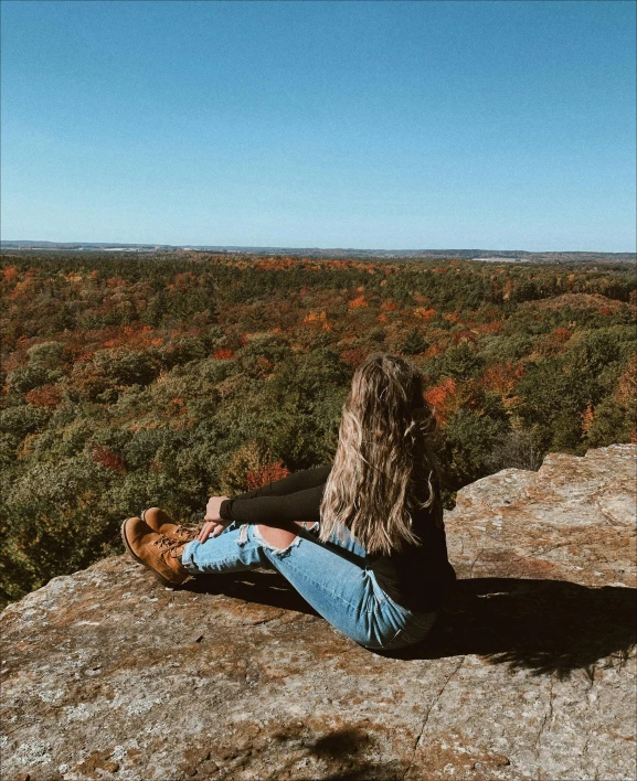 the woman is sitting on a cliff top overlooking the desert