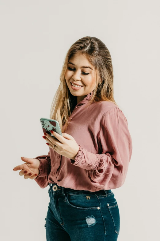 young woman standing against a white background and looking at her phone