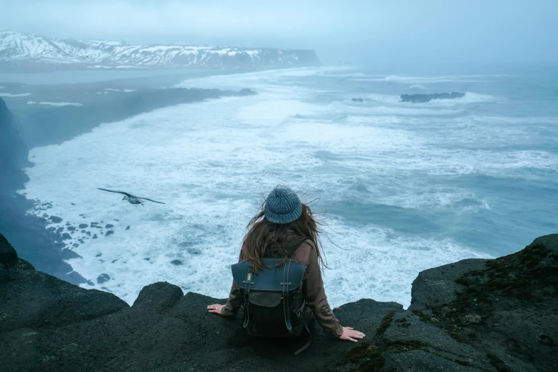 a girl is sitting on some rocks by the sea