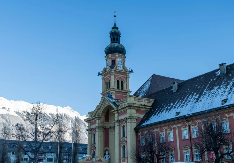 a building with a clock on it sits next to a snow covered mountain