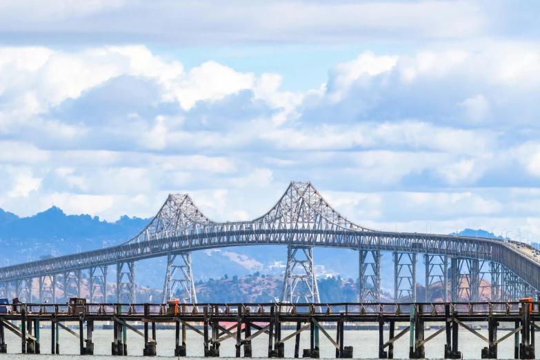 a pier with several poles and a large bridge in the background