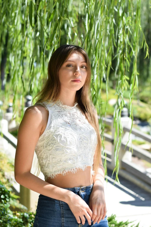 a woman with long hair in jeans is posing near a tree