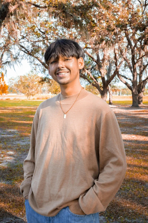 man wearing a tan sweater and blue jeans posing for a po