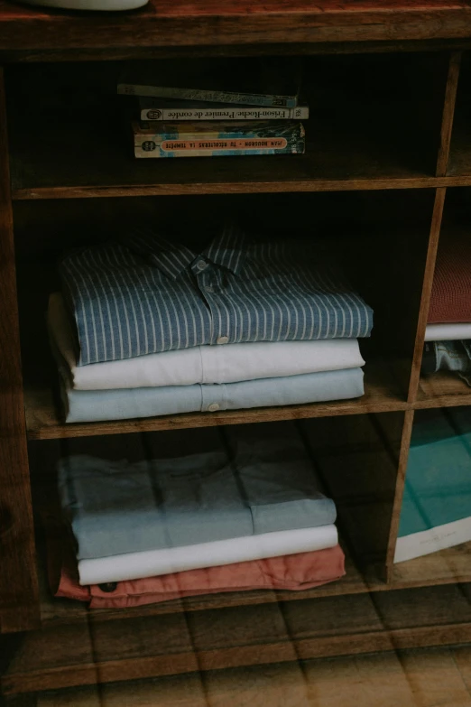 a wooden shelf filled with folded clothing and books