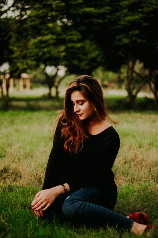 a woman sits in the grass looking into the distance