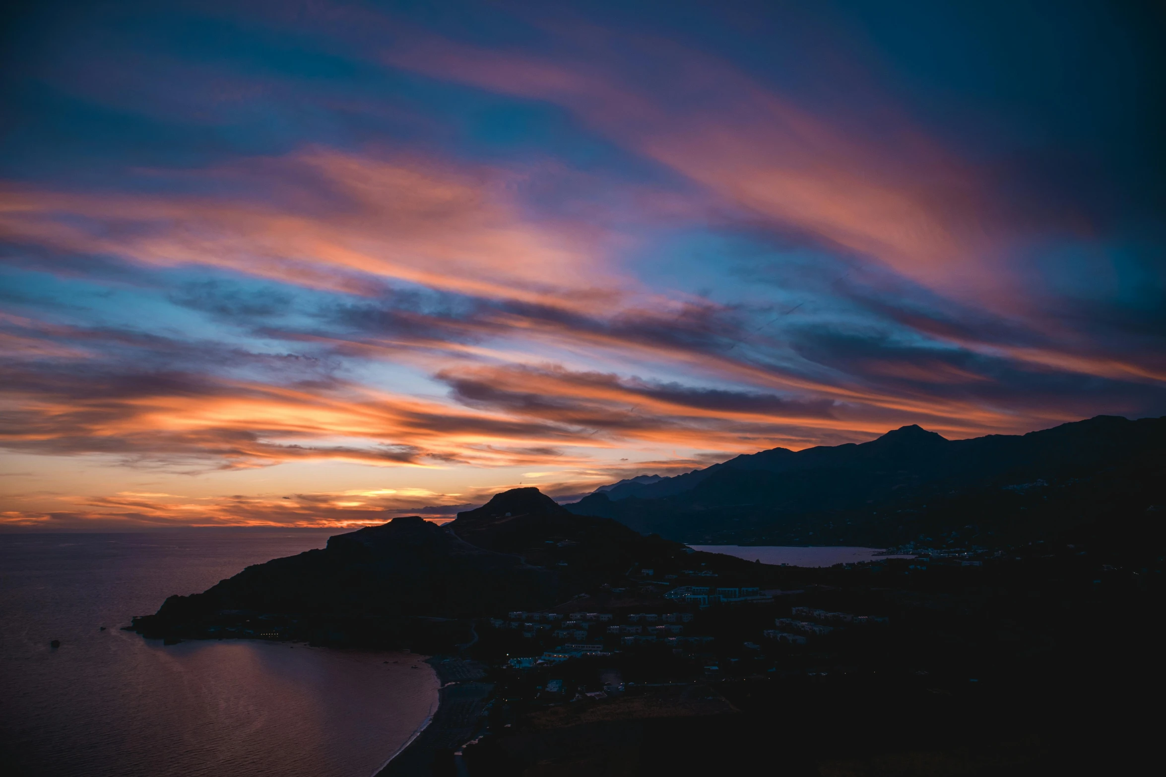 a view from a mountain of a body of water under a cloudy sky