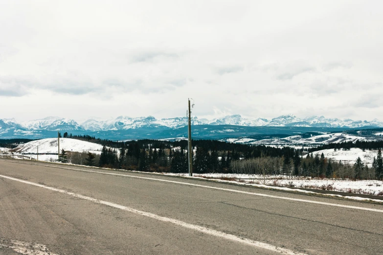 snow covered mountains and snowy roadway with a telephone pole