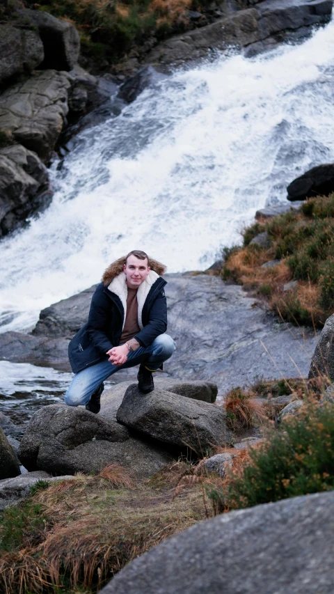 a person is posing for a picture on the rocks near a waterfall