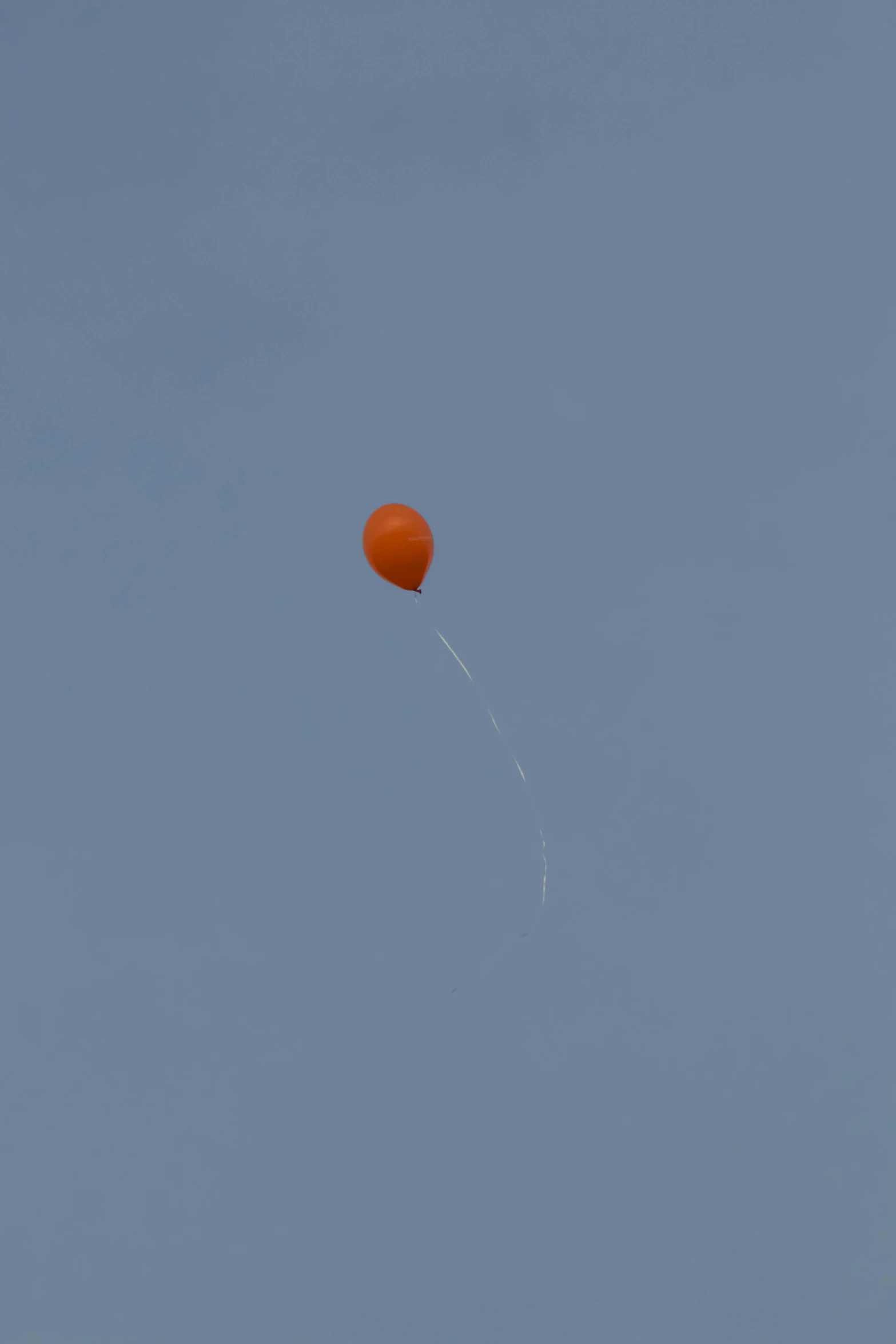 an orange kite with a string flying on a clear sky