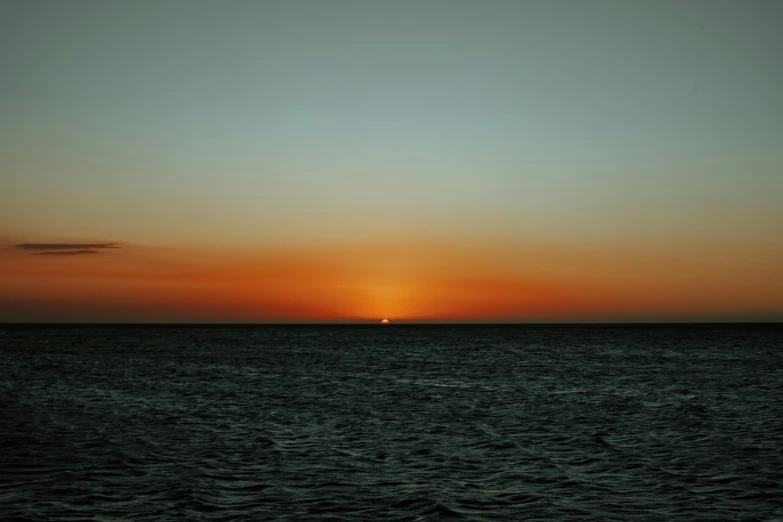 a boat floating on top of the ocean under a sunset