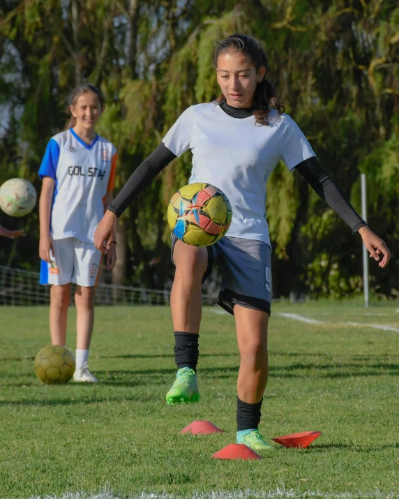 two girls playing soccer on a field near trees