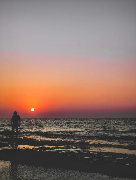 a person standing on the beach with a sunset behind them