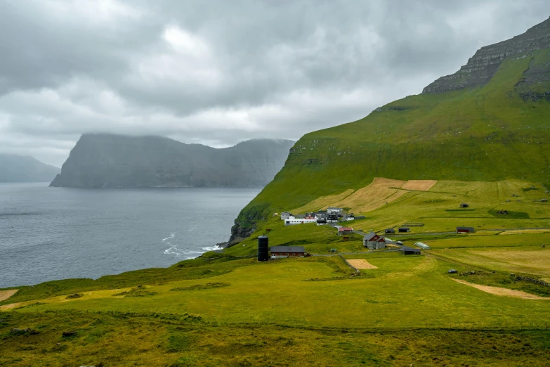 the green hillside and farm buildings stand at the edge of the ocean